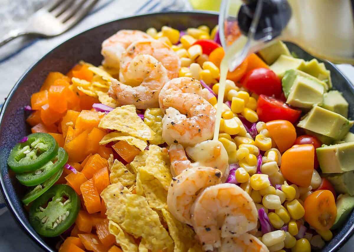 a colorful bowl of taco salad with shrimp being drizzled with cilantro lime dressing