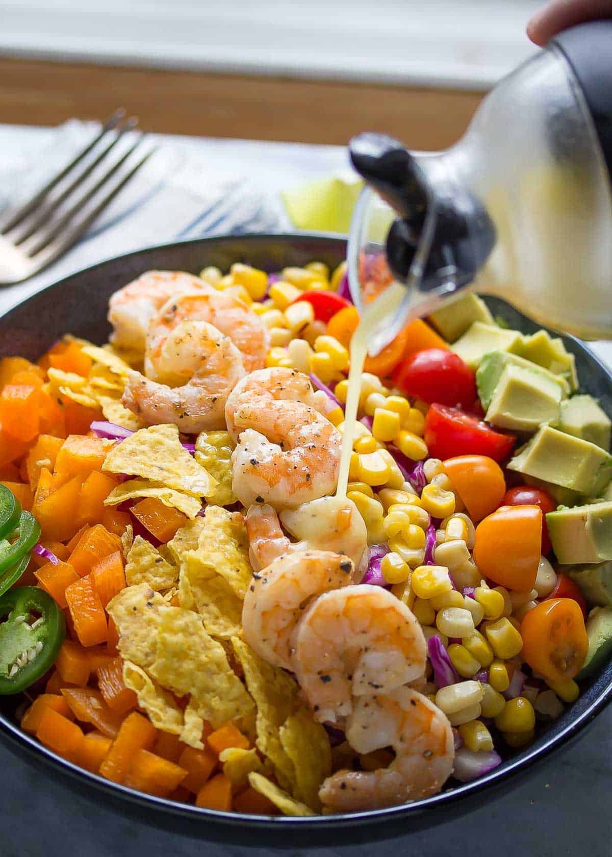 dressing being poured onto taco salad on black plate