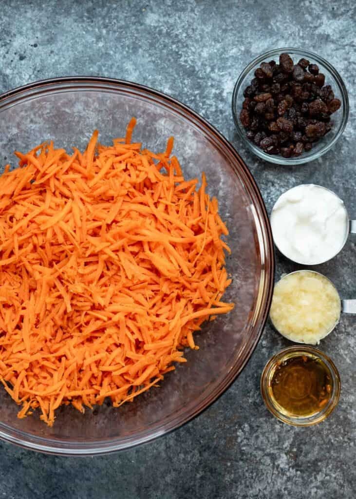all carrot raisin salad ingredients in separate bowls on a countertop
