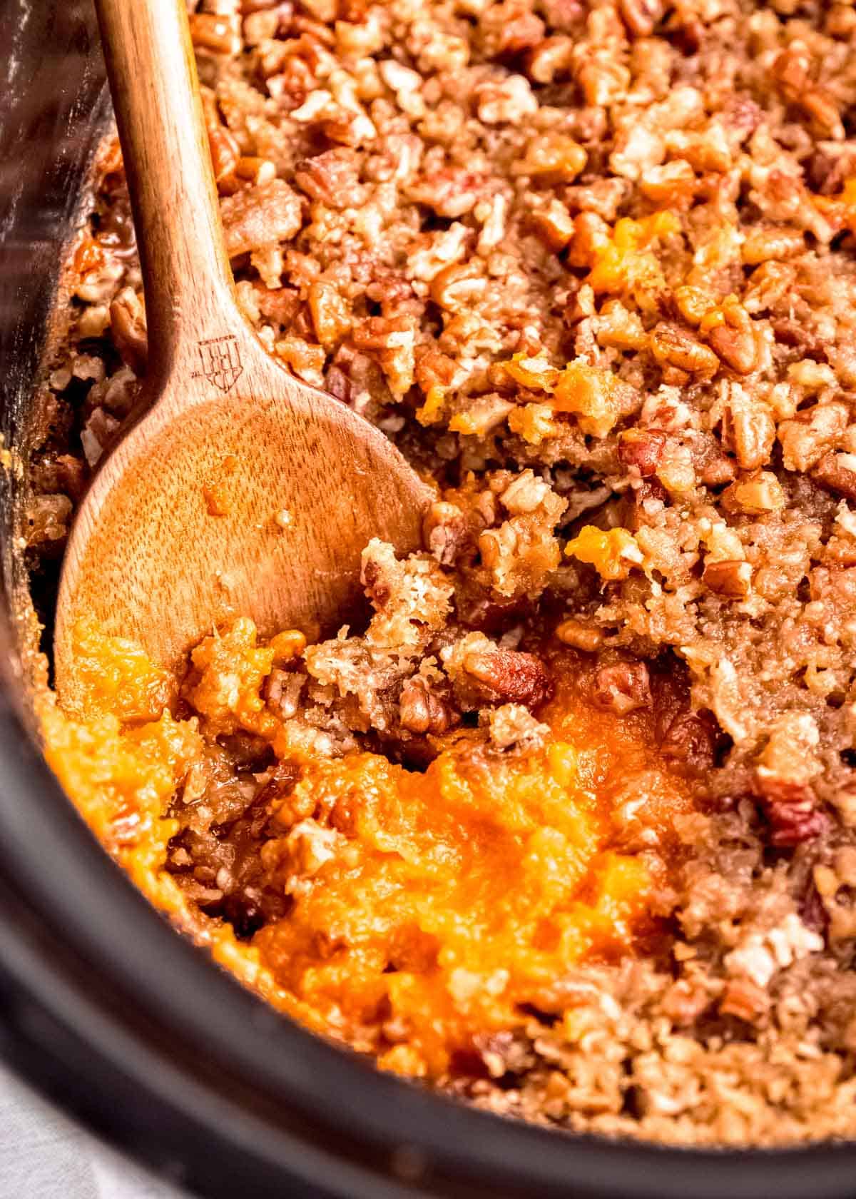 slow cooker sweet potato casserole in a black crockpot with a wooden spoon
