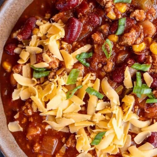 a closeup shot of turkey chili in a bowl with shredded cheese