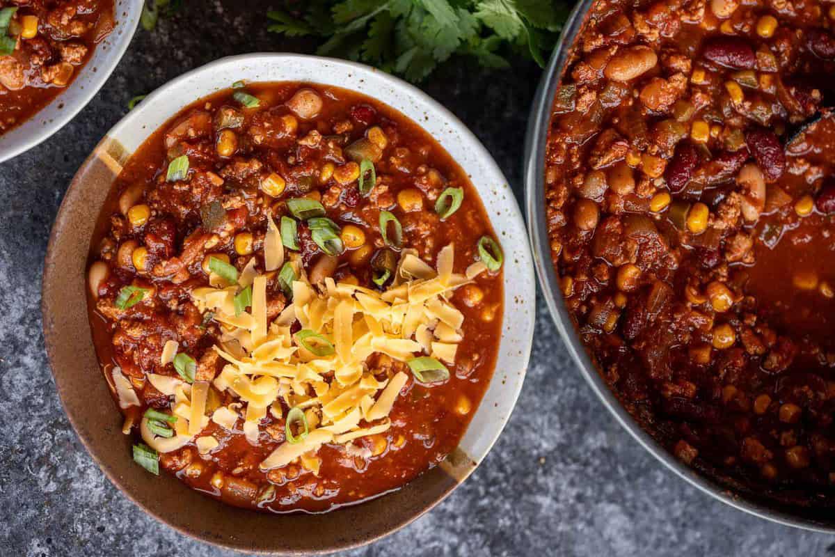 an overhead shot of a pot of turkey chili and a bowl of turkey chili with shredded cheese
