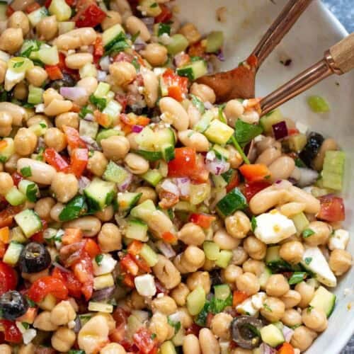 an overhead shot of a bean salad in a white bowl with tongs