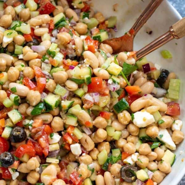 an overhead shot of a bean salad in a white bowl with tongs