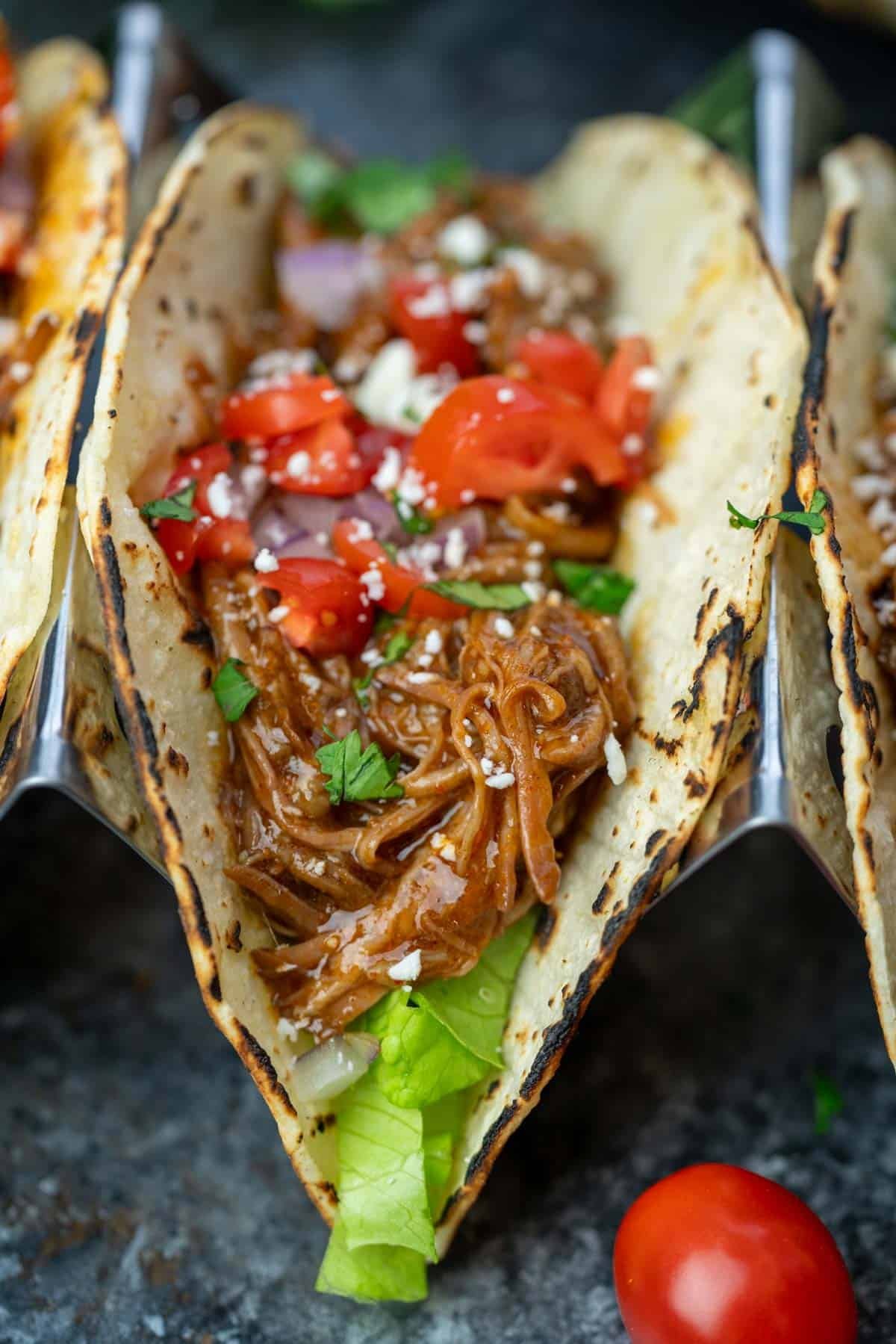 assembled shredded beef tacos with tomatoes, herbs, and cheese