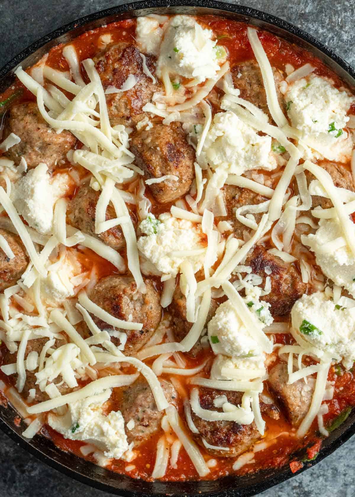 meatballs and a cheesy mixture distributed throughout the skillet of tomato sauce, all topped with shredded mozzarella cheese