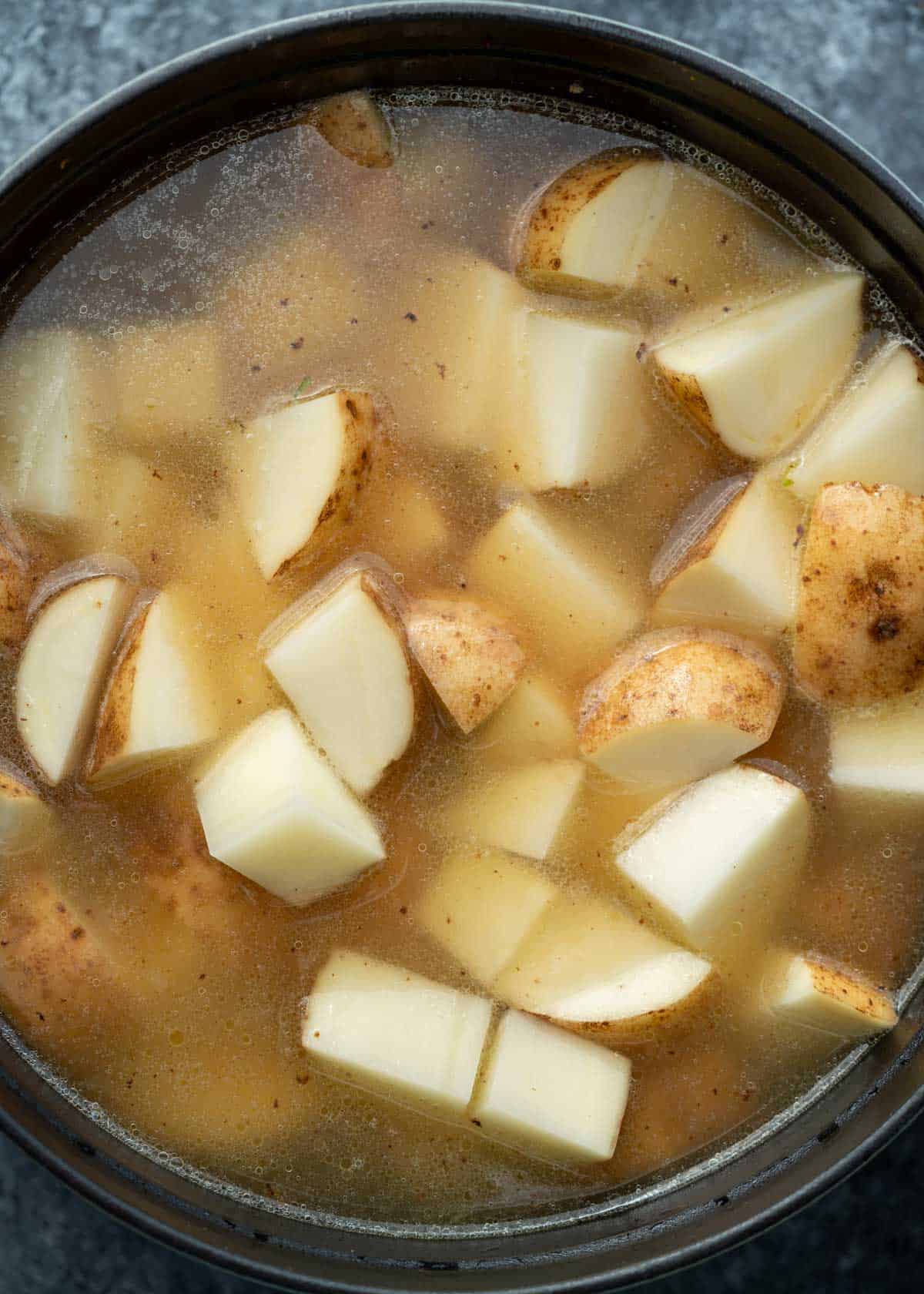 potatoes in a pot with veggies, broth, and seasonings