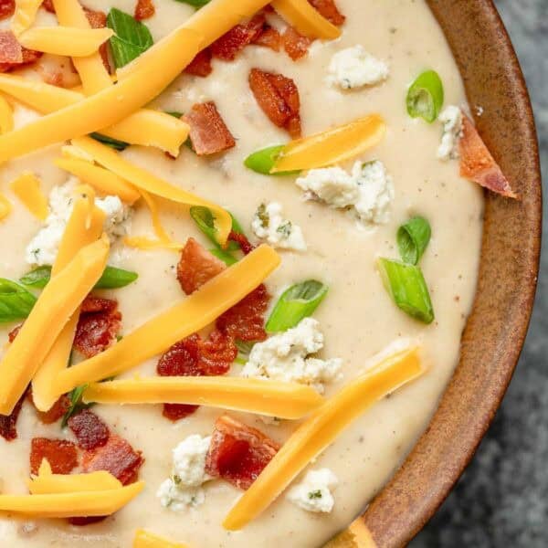 a bowl full of creamy boursin potato soup, topped with cheddar, boursin, bacon, and green onions