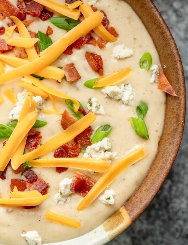 a bowl full of creamy boursin potato soup, topped with cheddar, boursin, bacon, and green onions