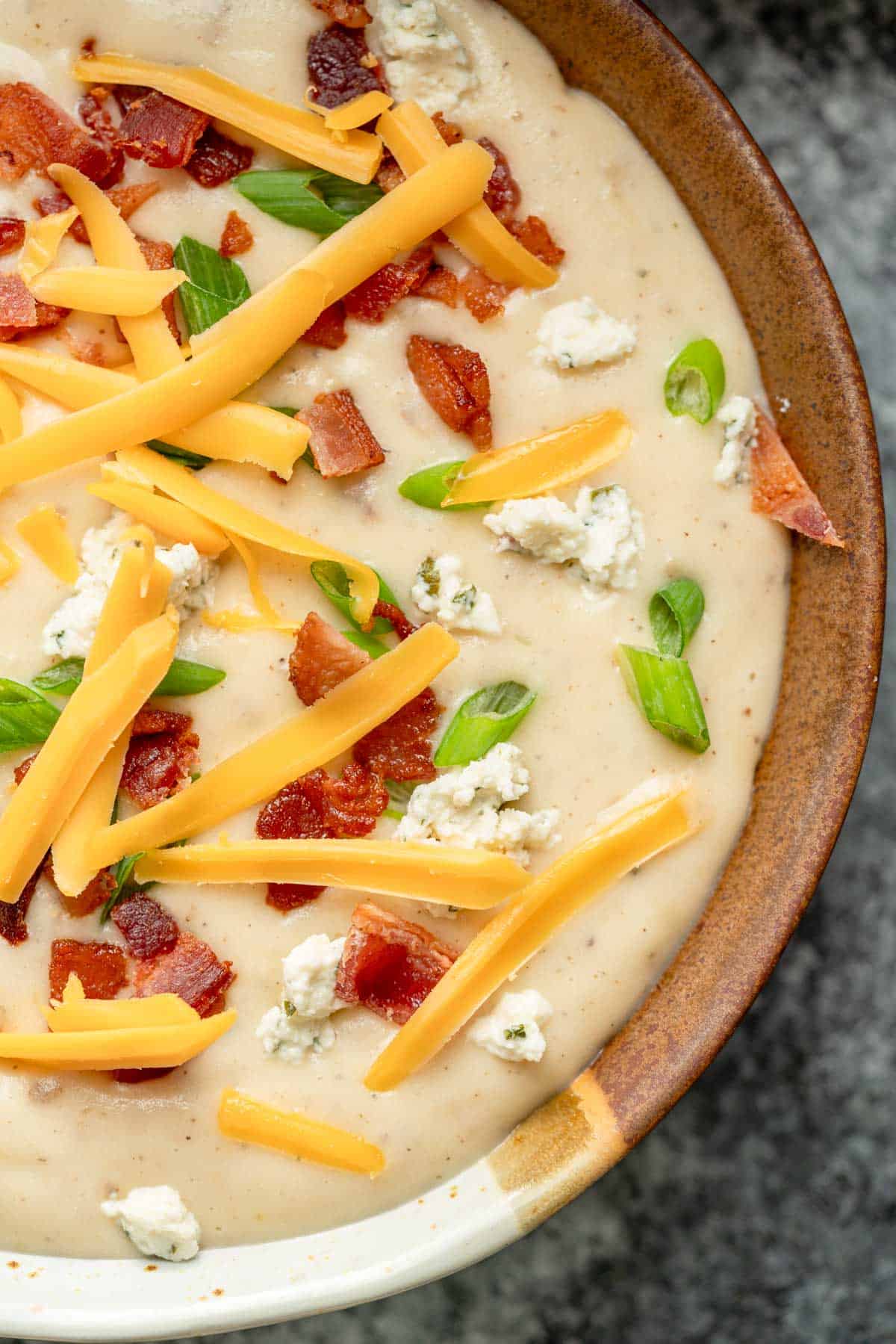 a bowl full of creamy boursin potato soup, topped with cheddar, boursin, bacon, and green onions