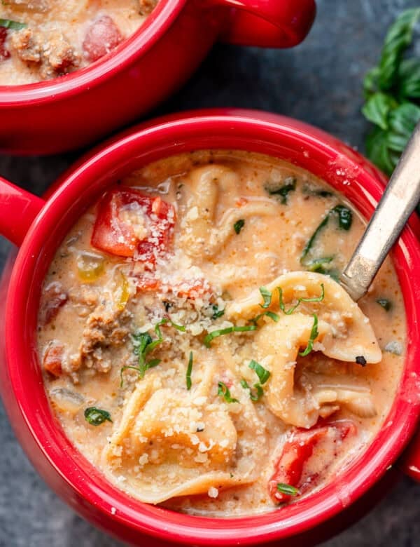 a red bowl of creamy tortellini soup with basil on top