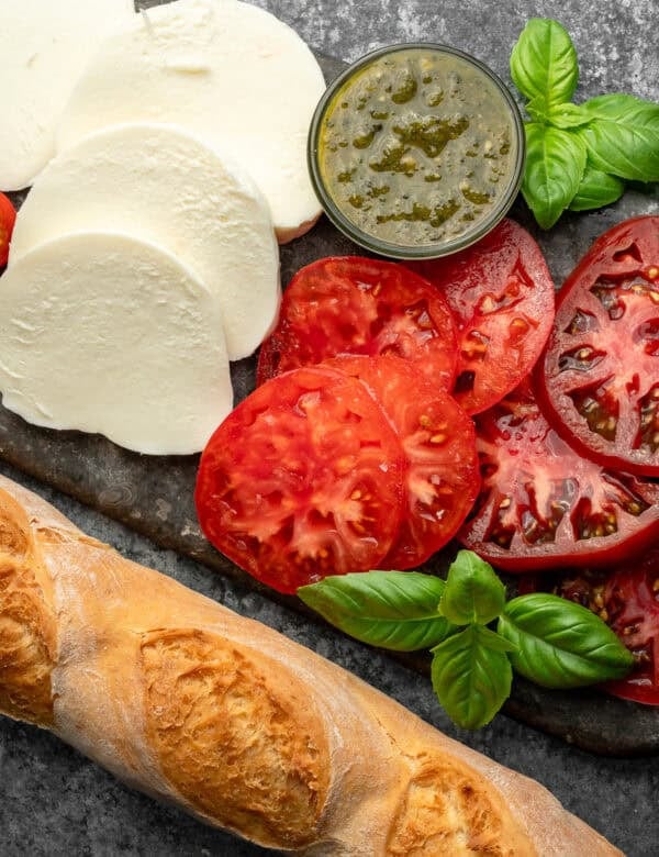 overhead image of sliced tomatoes, mozzarella, and a baguette on a stone cutting board