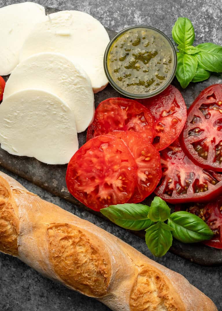 overhead image of sliced tomatoes, mozzarella, and a baguette on a stone cutting board