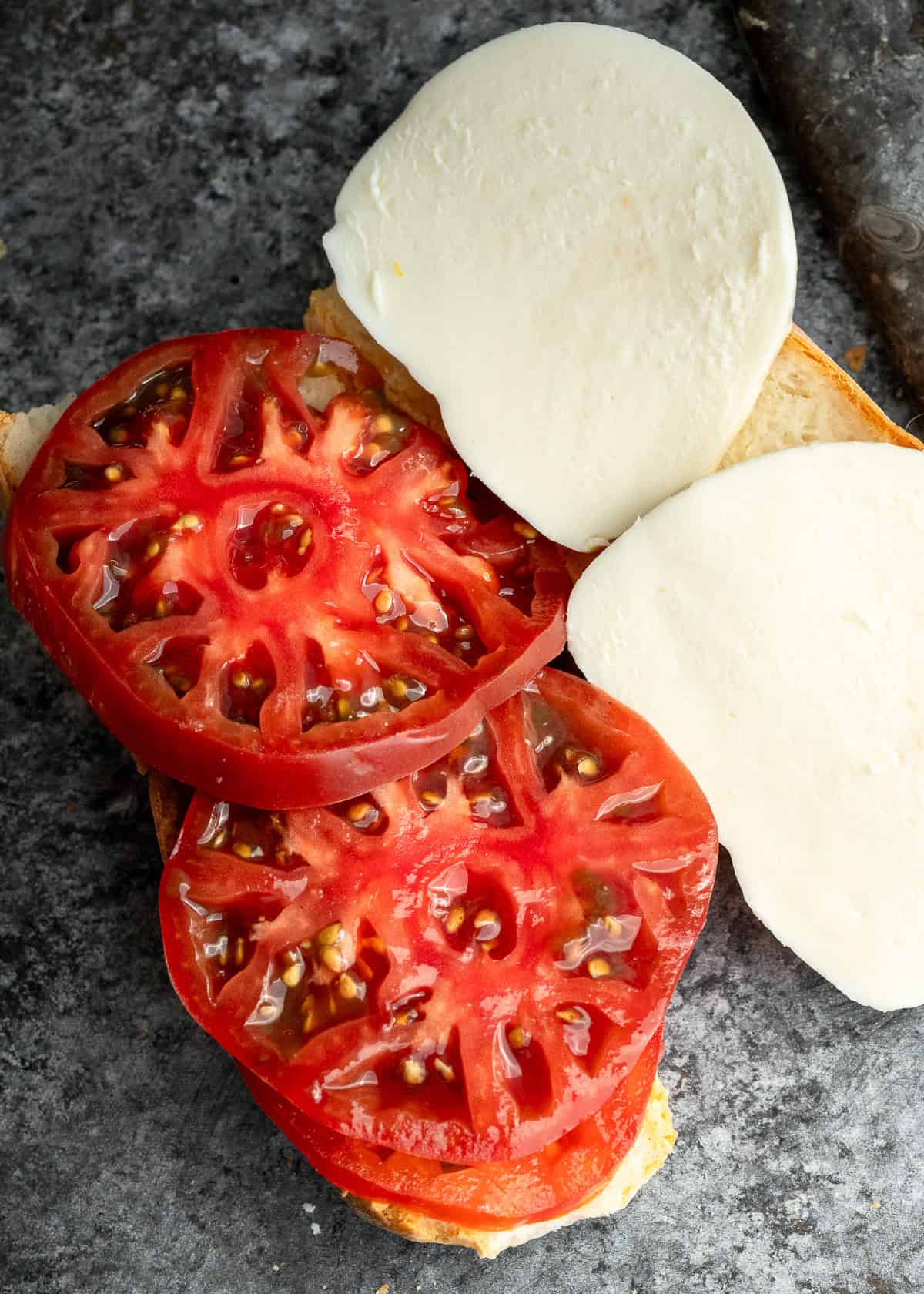 tomatoes and mozzarella on a baguette on a stone cutting board
