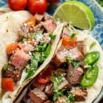 overhead image of carne asada tacos on a blue plate with a lime and tomatoes