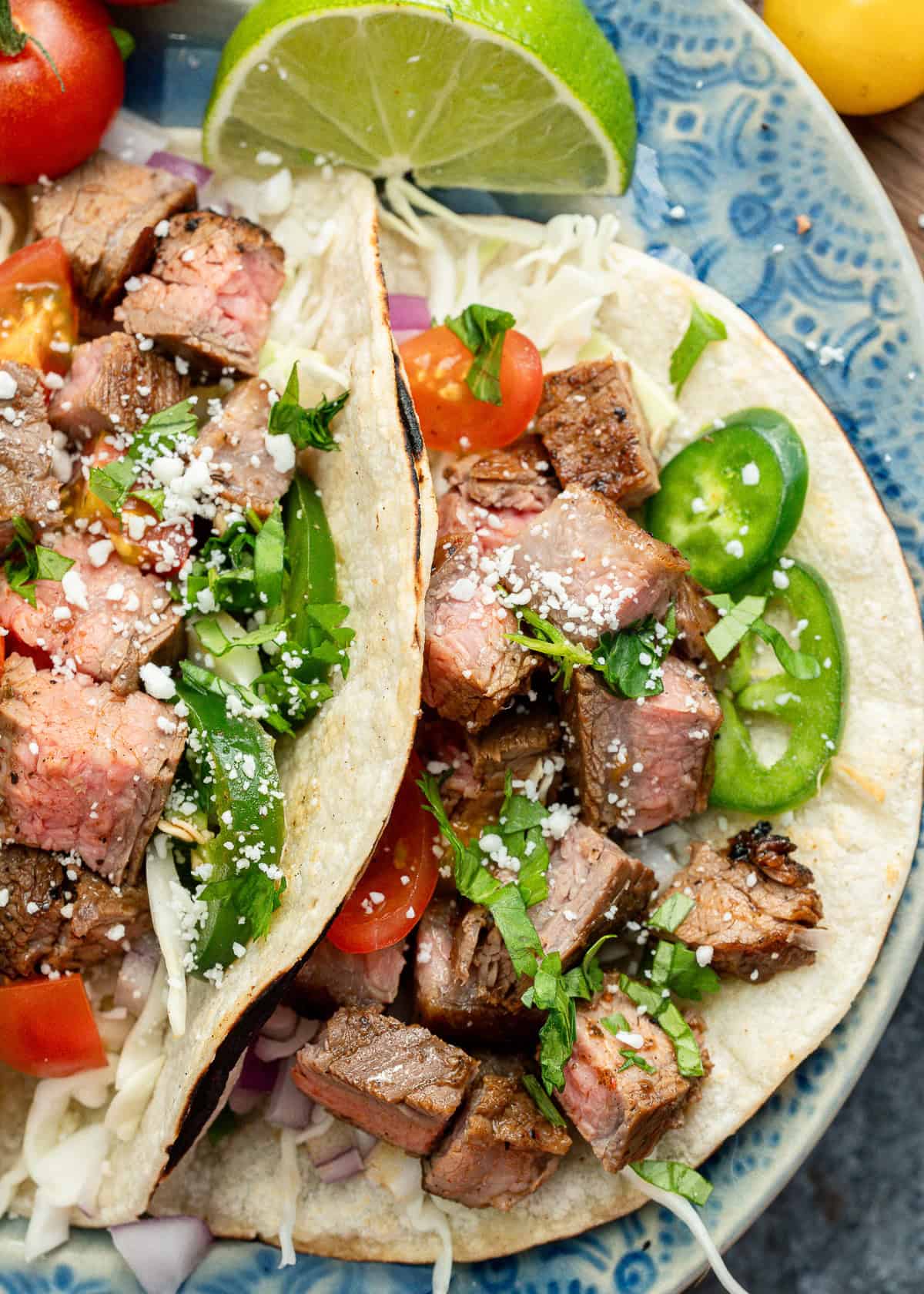 overhead image of two carne asada tacos on a blue plate