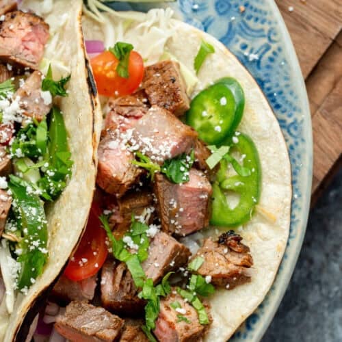 overhead image of two carne asada tacos on a blue plate with jalapenos