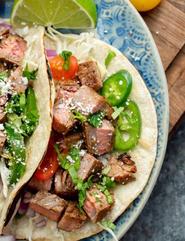 overhead image of two carne asada tacos on a blue plate with jalapenos