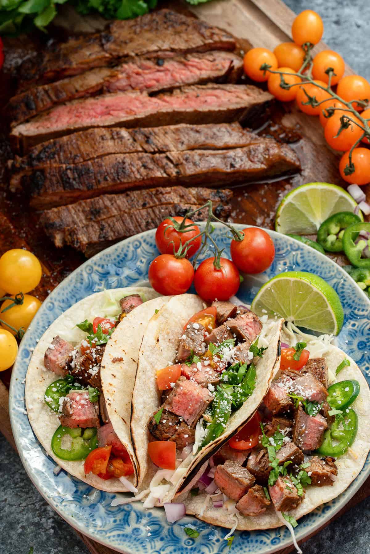 overhead image of a plateful of carne asada tacos with sliced carne asada in the background