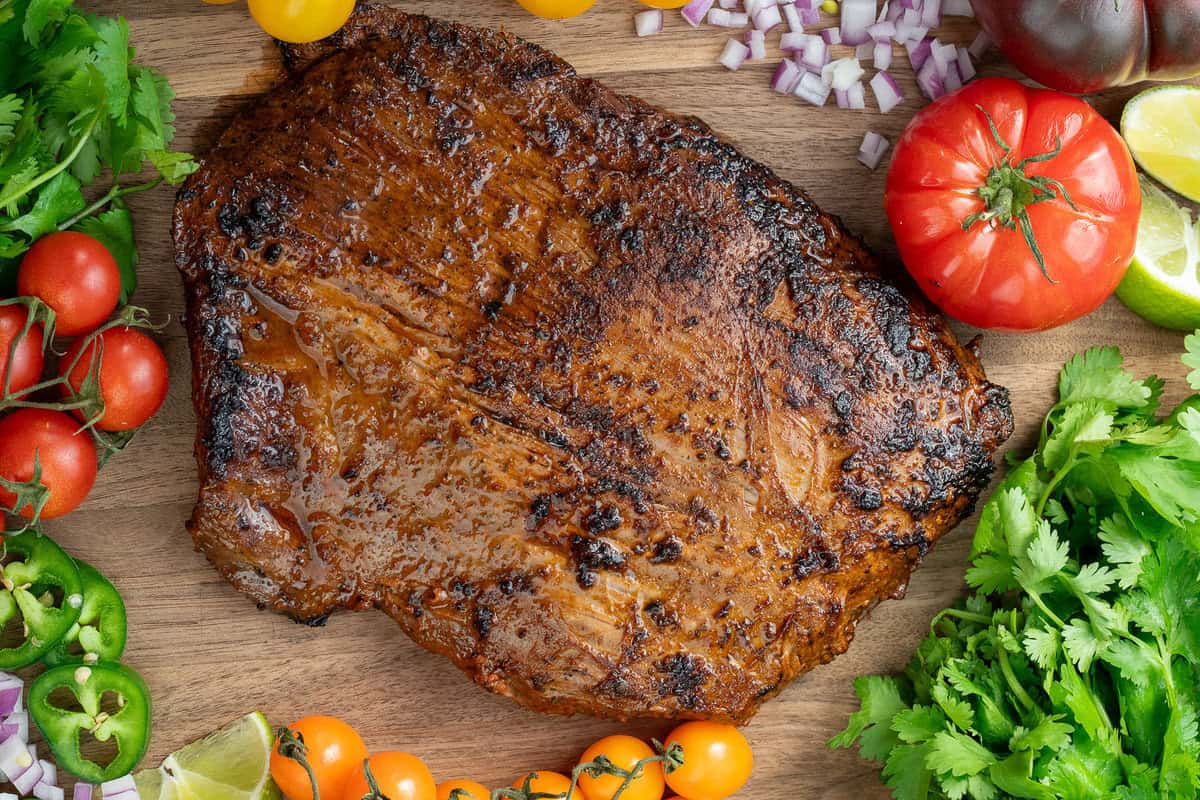 cooked, unsliced carne asada on wooden cutting board