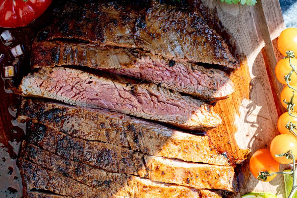 overhead image of sliced carne asada on wooden cutting board with sun shining across cutting board