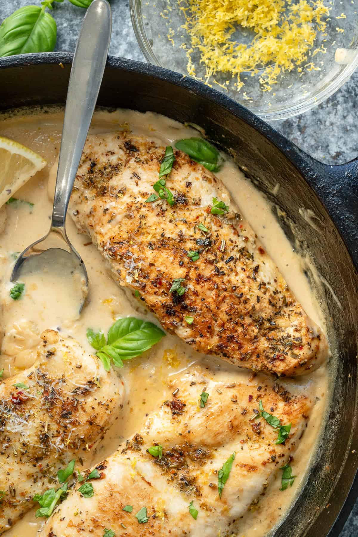 overhead image of lemon garlic chicken and a lemon in a creamy sauce in a cast iron skillet