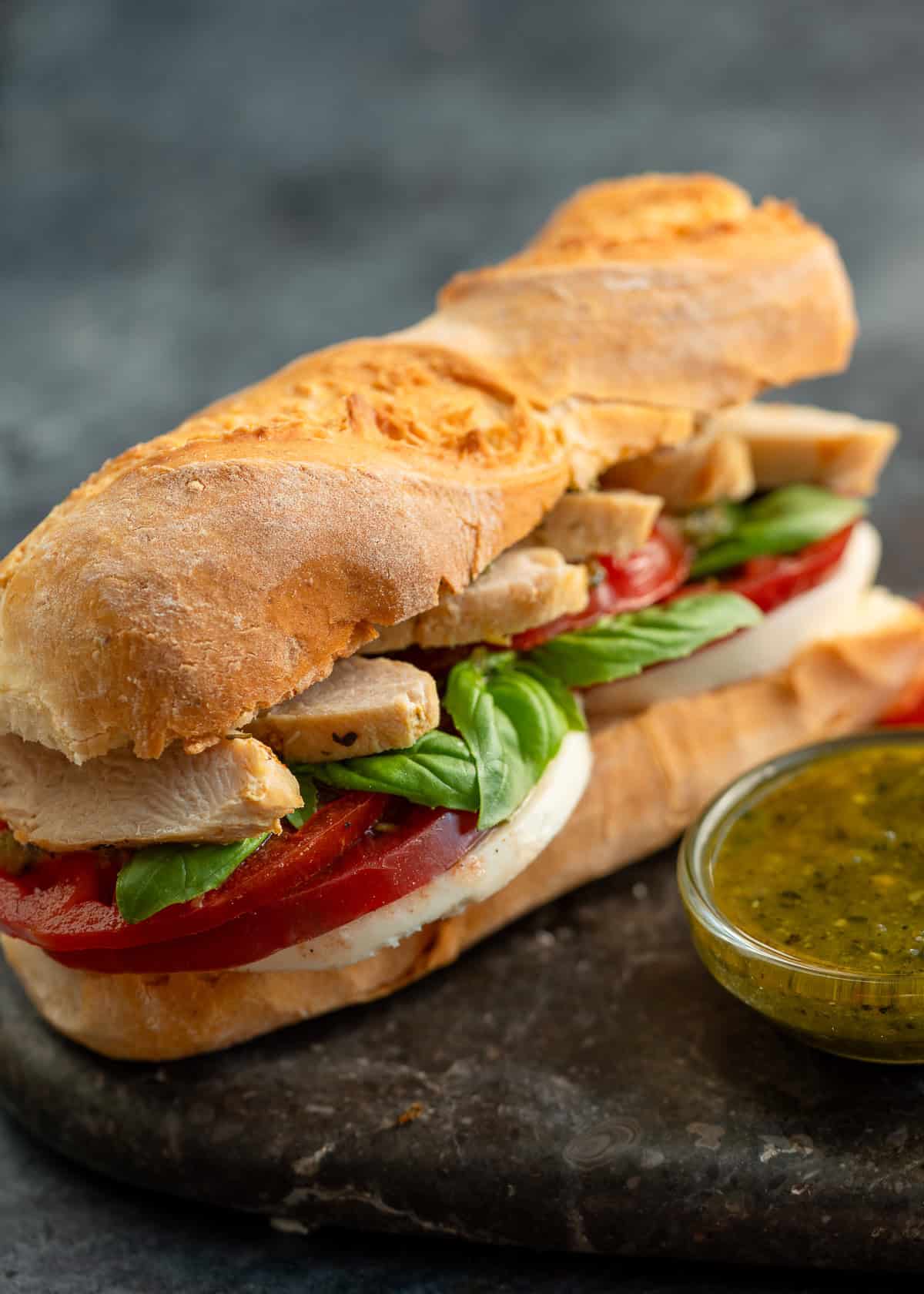 pesto chicken sandwich and pesto sauce on a stone countertop