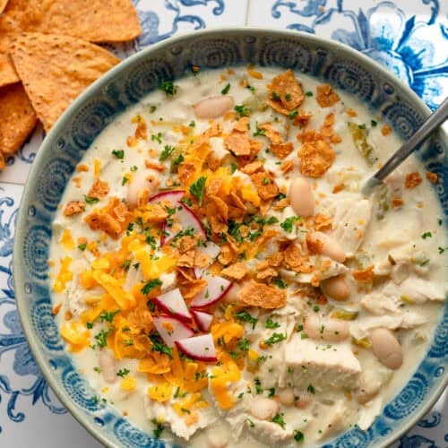 overhead image of white bean chili in blue bowl with spoon on decorative background