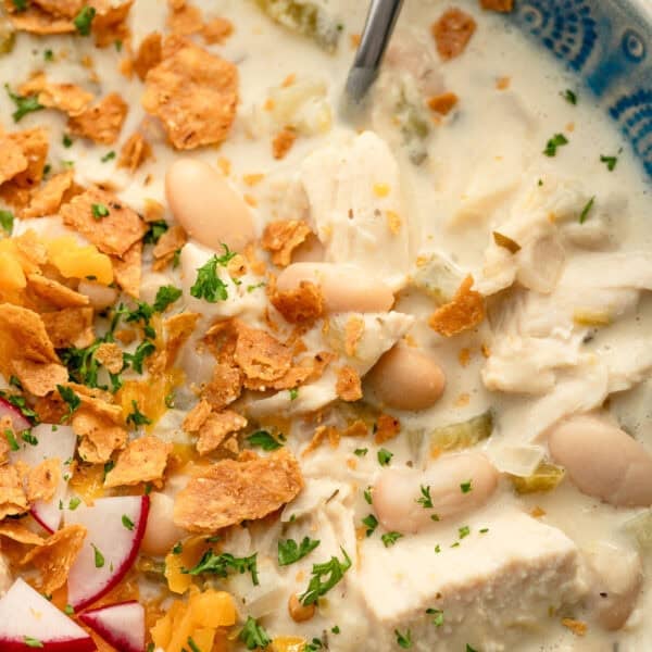 close up image of white bean chili and silver spoon in blue bowl