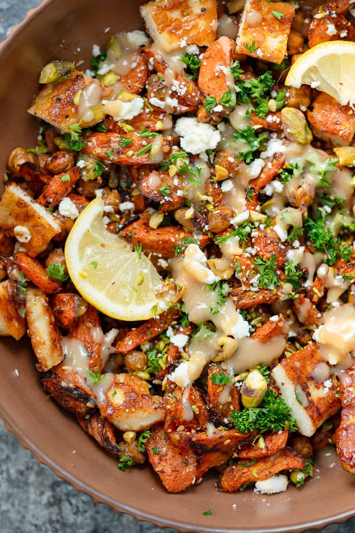 an overhead shot of hot honey halloumi salad with carrots, chickpeas and lemon in a brown bowl