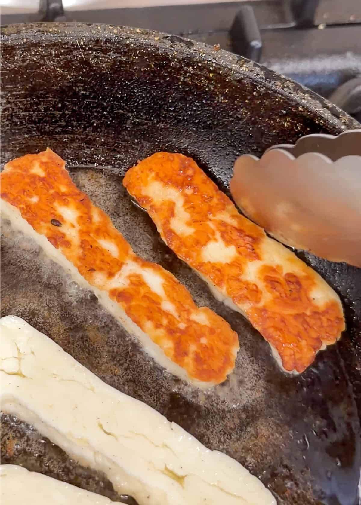 halloumi being turned in a skillet with tongs