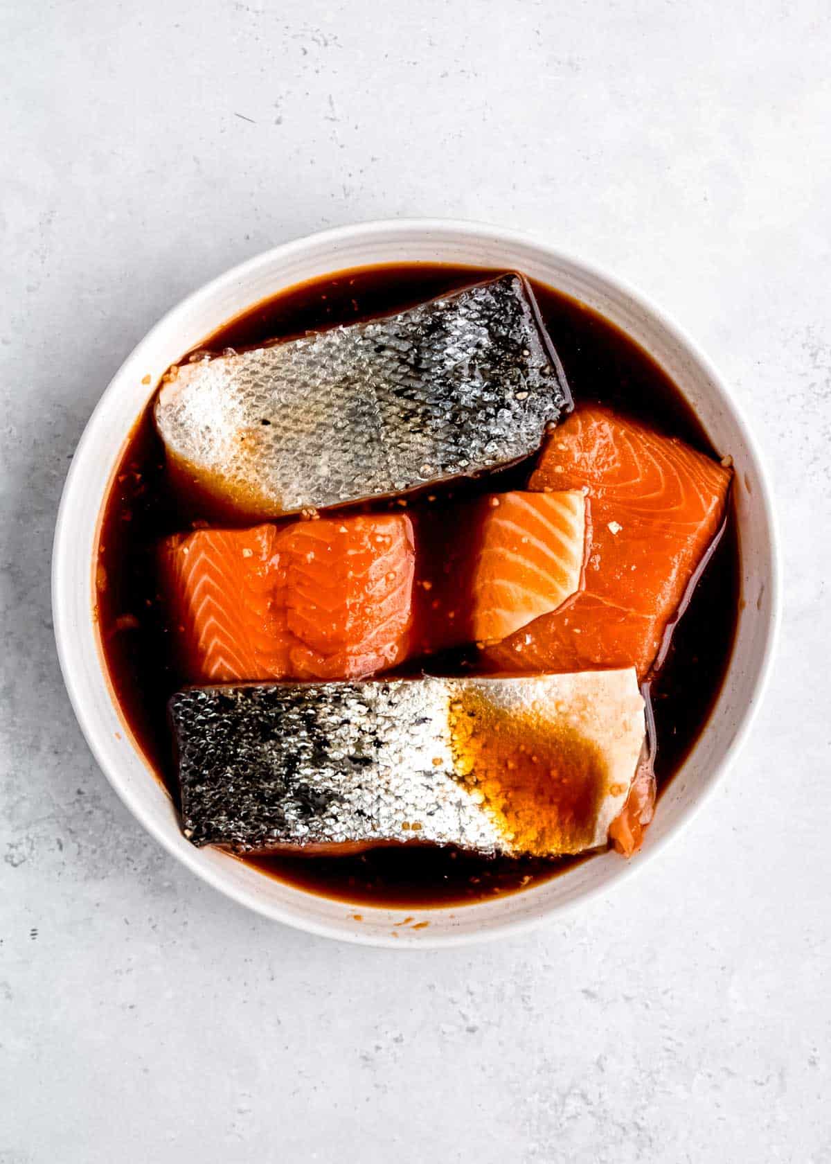 salmon marinating in teriyaki sauce in a white bowl