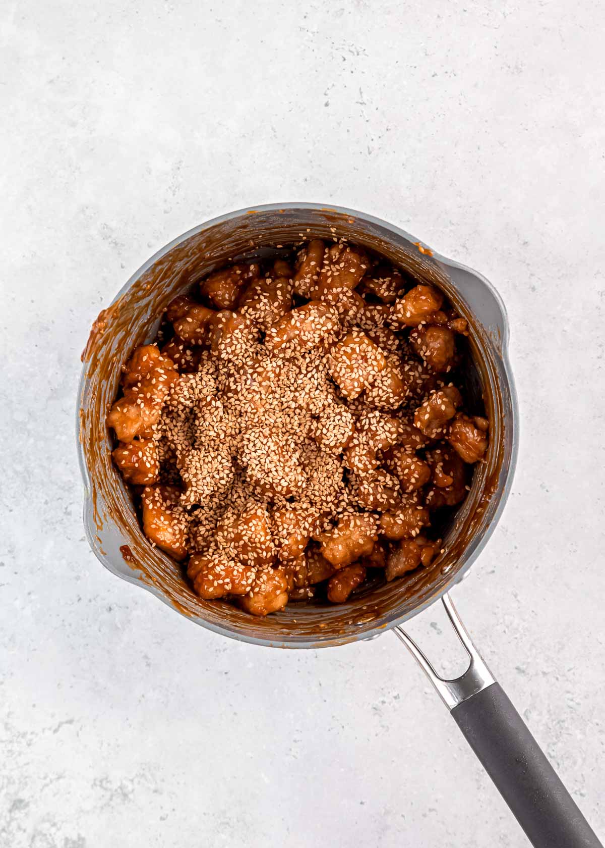 fried chicken tossed into a sauce pan with honey sesame sauce and sesame seeds