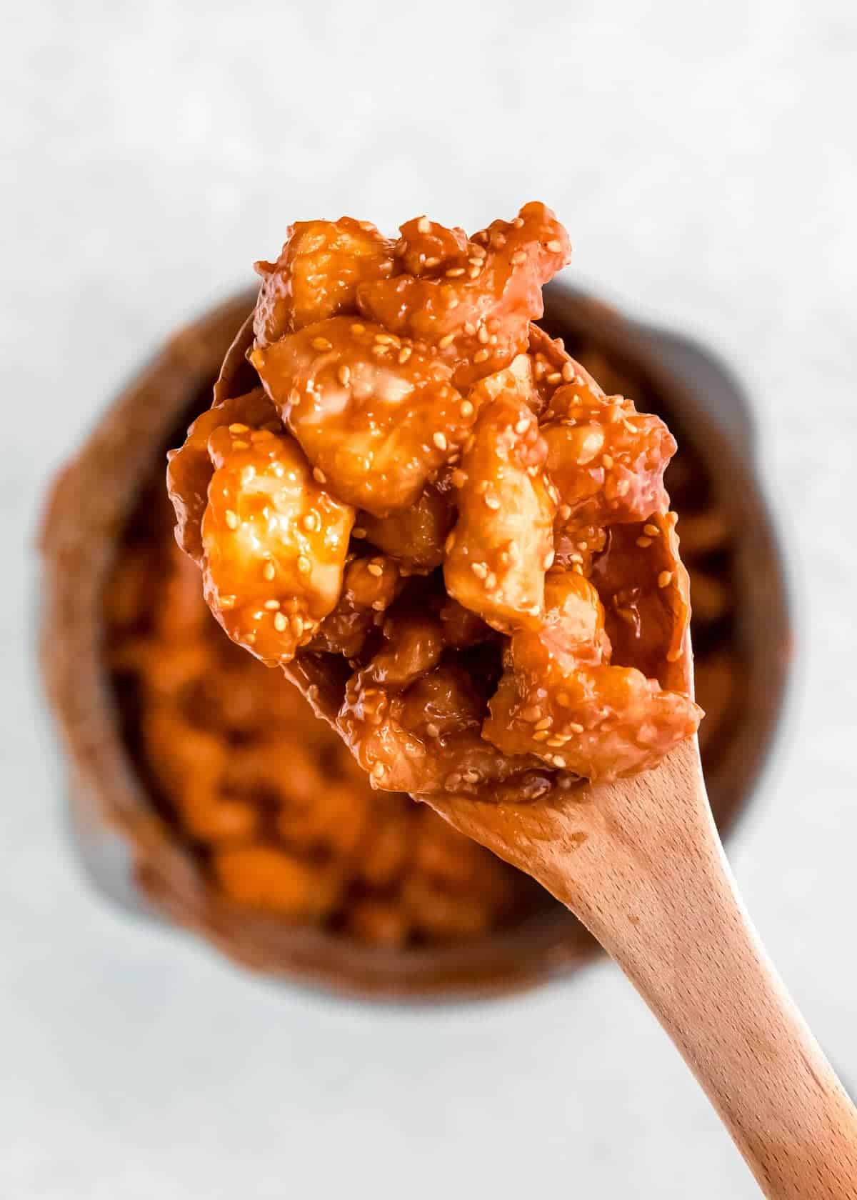 a wooden spoon full of crispy, saucy sesame chicken