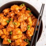 black bowl filled with sticky sesame chicken garnished with sesame seeds and green onions