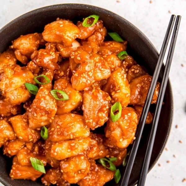 black bowl filled with sticky sesame chicken garnished with sesame seeds and green onions