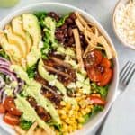 southwest chicken salad in a white bowl on a white table with a fork and cotija cheese
