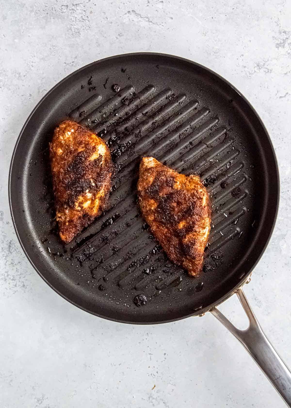 two chicken breasts cooking in a skillet