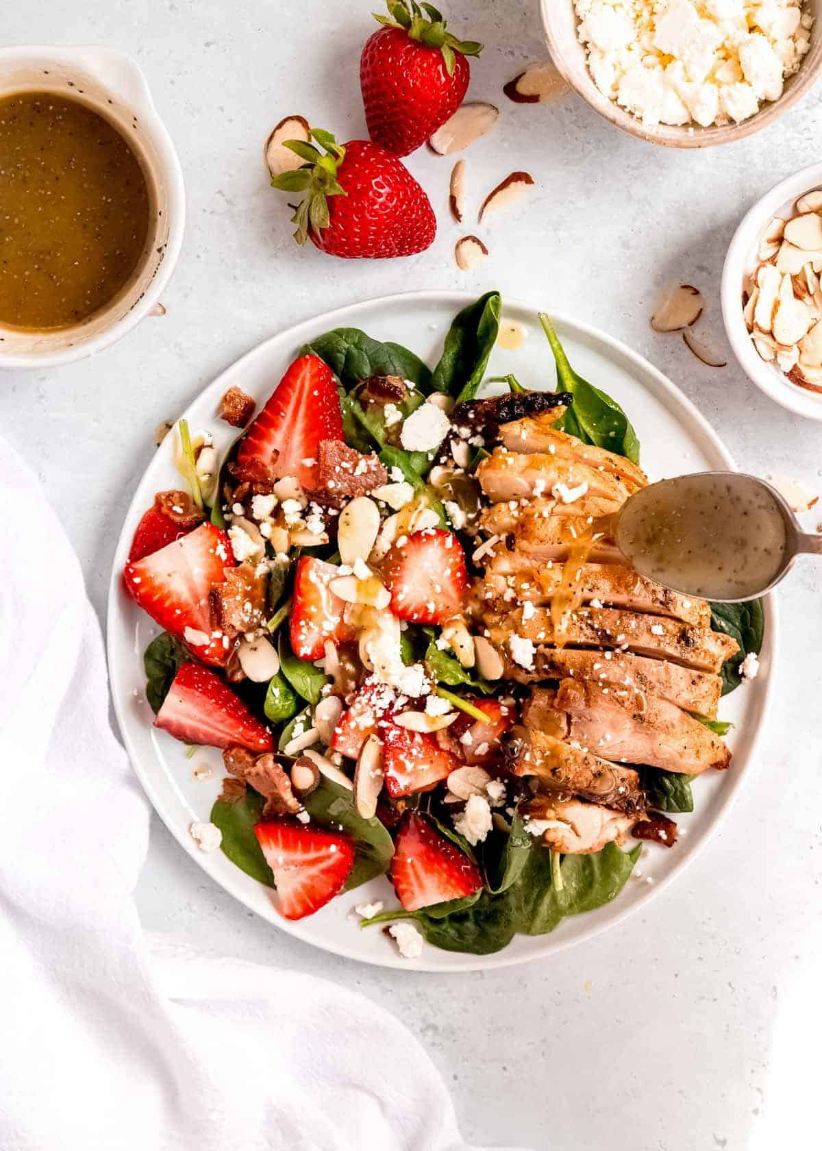 salad dressing being drizzled on strawberry spinach salad