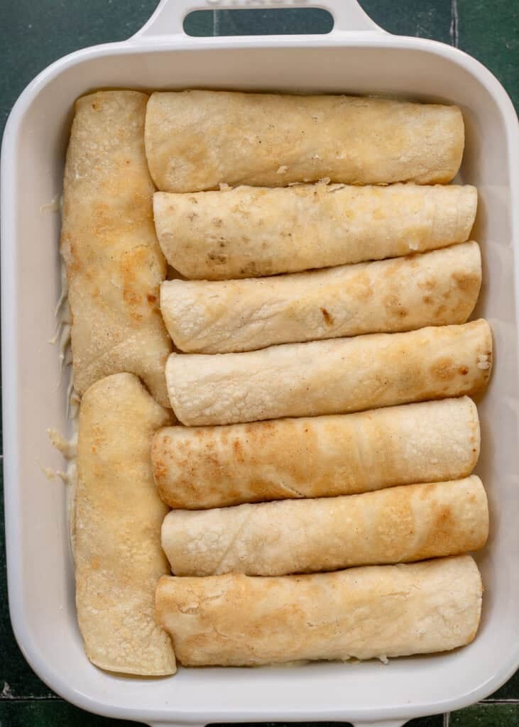 green chili chicken enchiladas rolled in a baking dish prior to topping with cheese