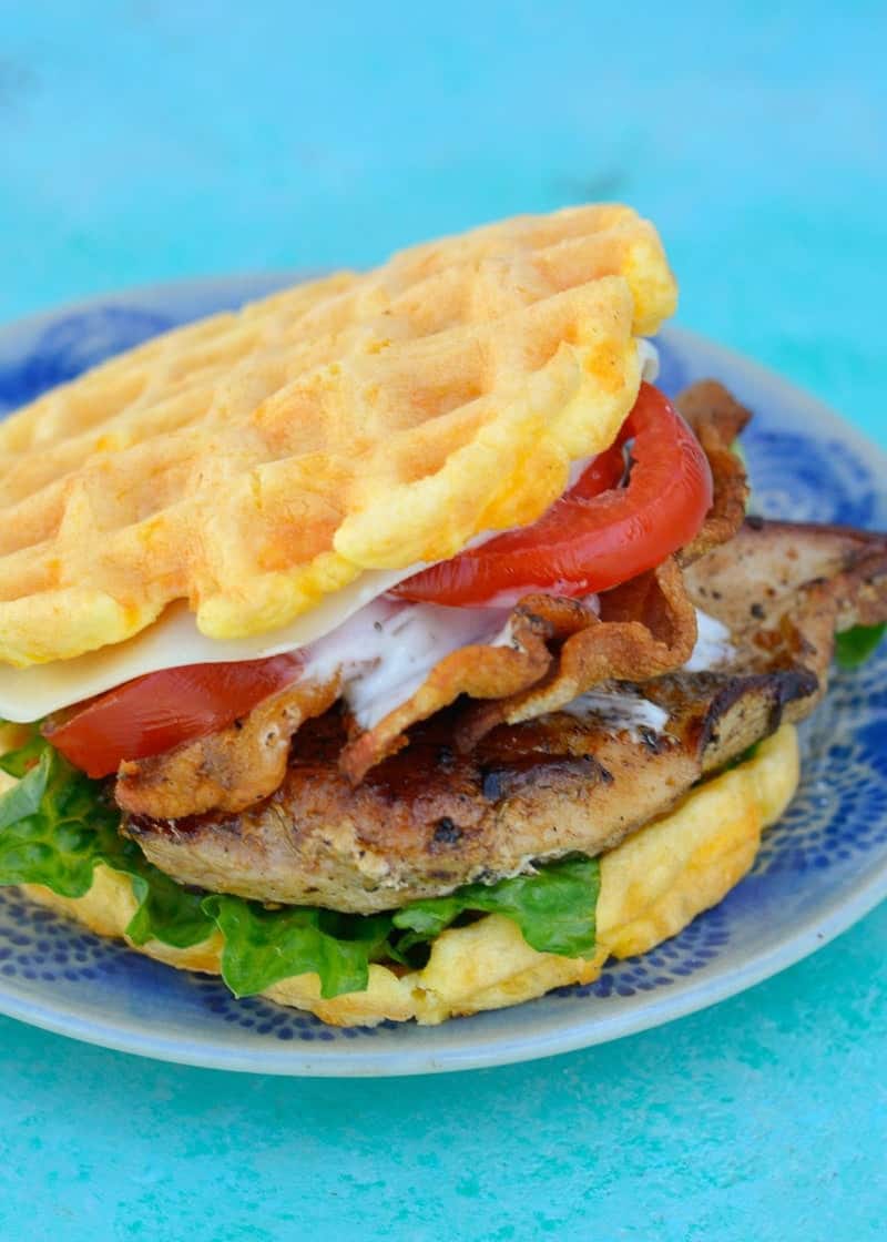 two chaffles filled with a grilled chicken breast, crispy bacon, tomato, cheese, lettuce, and ranch