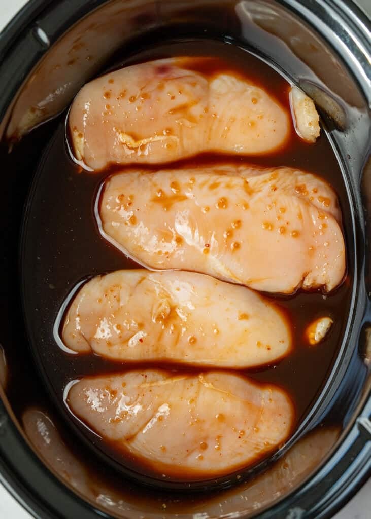 an overhead shot of uncooked chicken in a slow cooker