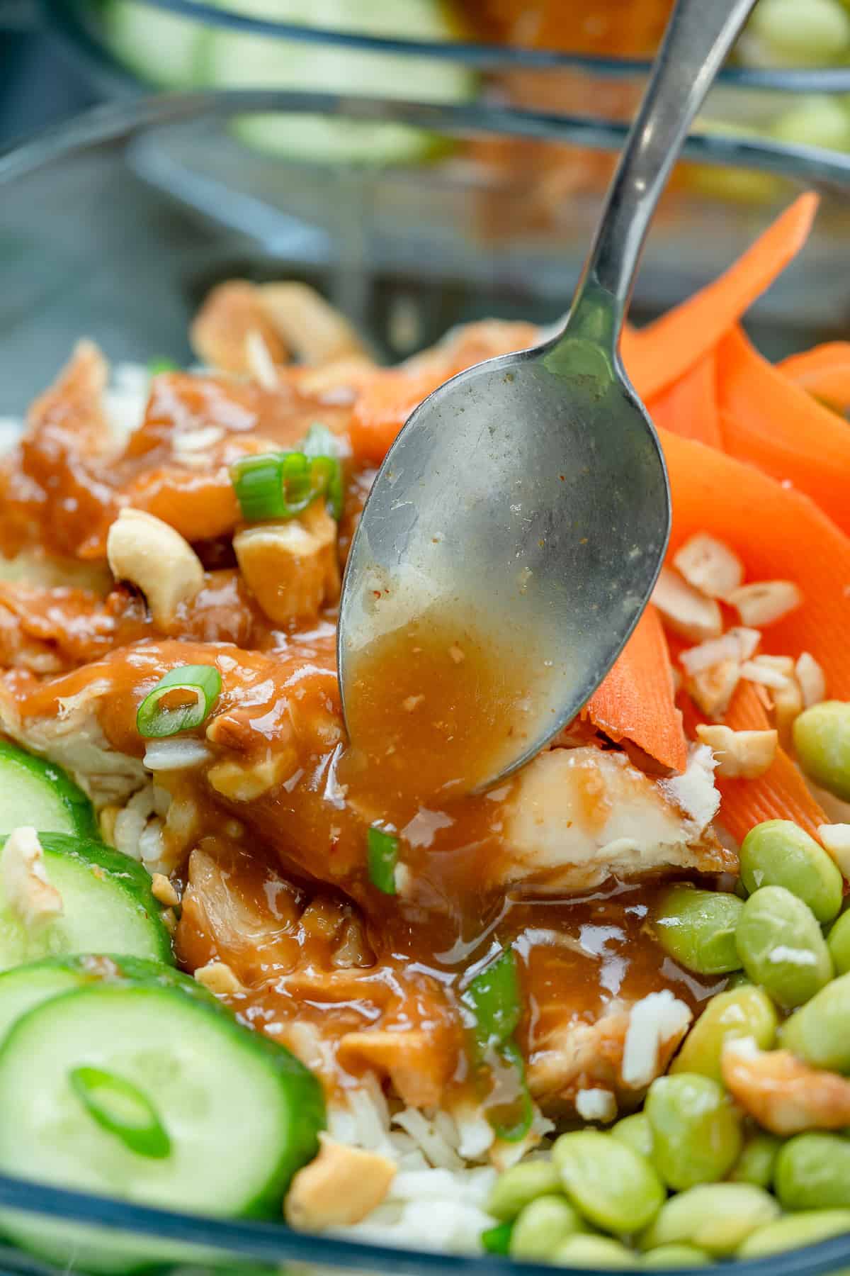 a shot of sweet chili sauce being drizzled over meal prep bowls